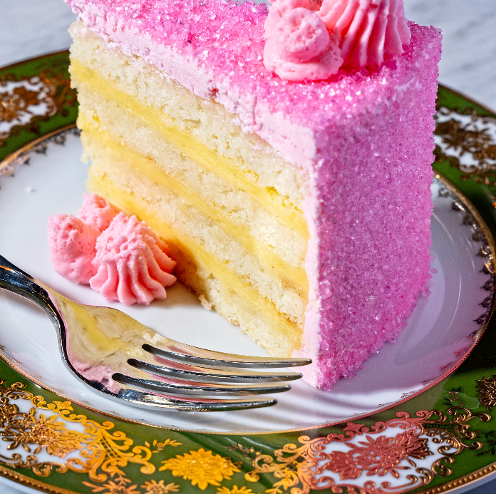 Slice of layered white cake with lemon filling and pink frosting coating, garnished with pink rosettes, served on ornate plate