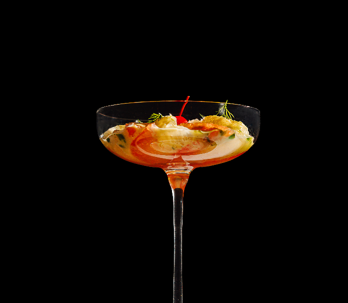 A coupe glass holding a savory appetizer garnished with herbs and a red accent against a black background.