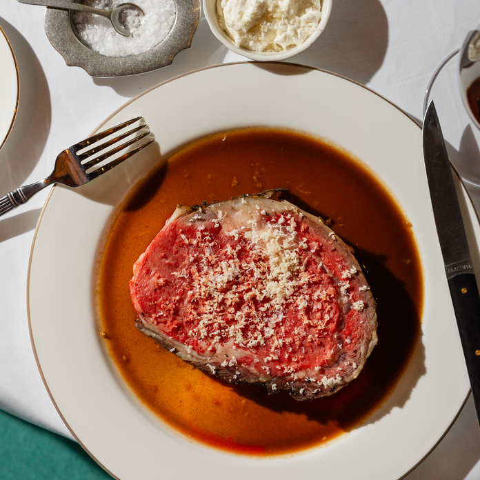 Seared steak on a white plate with brown sauce, grated cheese, and side of butter.