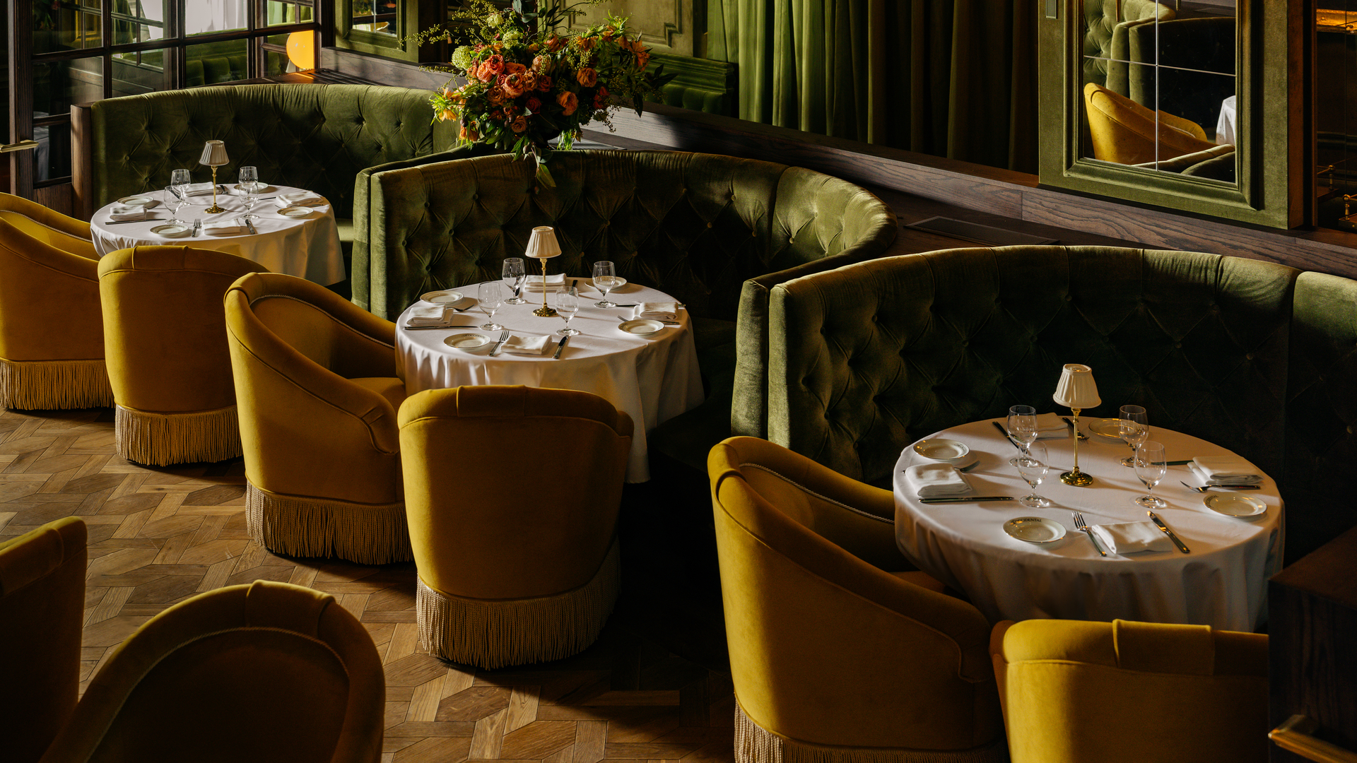 Elegant restaurant interior with plush mustard-yellow chairs, round tables set with white linens, and floral arrangements.